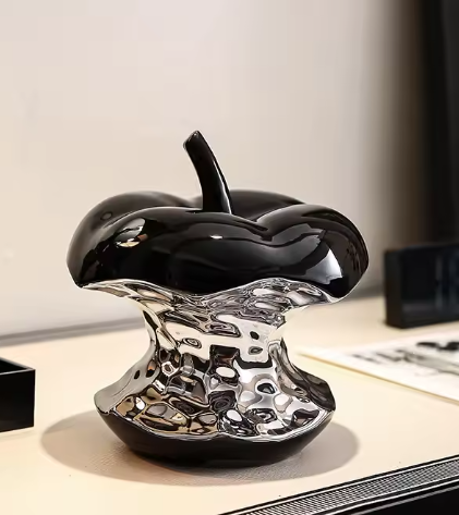 Electroplated ceramic apple ornament with glossy black top and chrome silver base on a desk