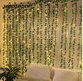 Warm white fairy string lights woven through artificial ivy vine garlands draped across a bedroom wall above a white bed