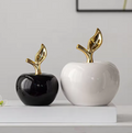 Black and white ceramic apple sculptures with gold stems displayed on a white shelf