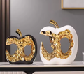 Gold-plated hollow apple ceramic sculptures in black and white displayed on a marble surface