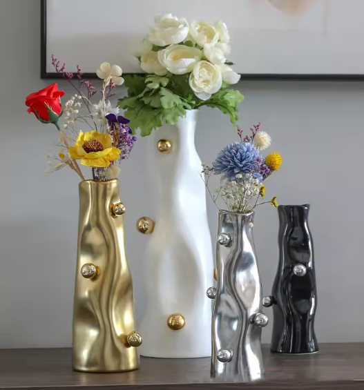 Four sculptural resin vases in gold, white, silver and charcoal with metallic sphere orbs holding colourful flowers